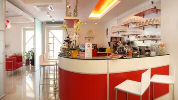 Uma área de recepção moderna com balcão de vidro, detalhes em vermelho e uma máquina de café.