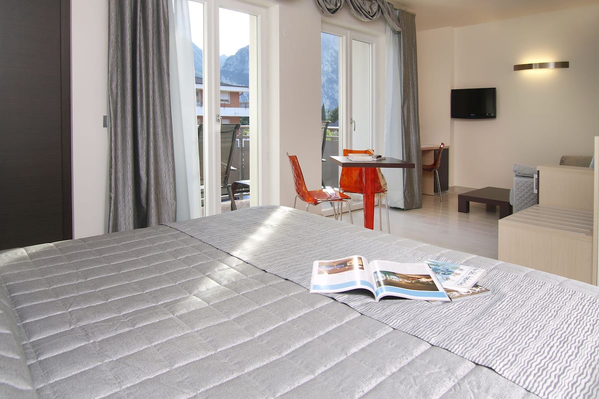 Habitación de hotel con cama, una mesa con sillas, un televisor y vistas a las montañas por la ventana.
