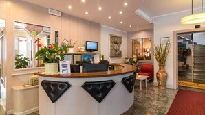 A reception area with a curved counter, a television, and various plants. - Hotel Miorelli (Nago-Torbole)