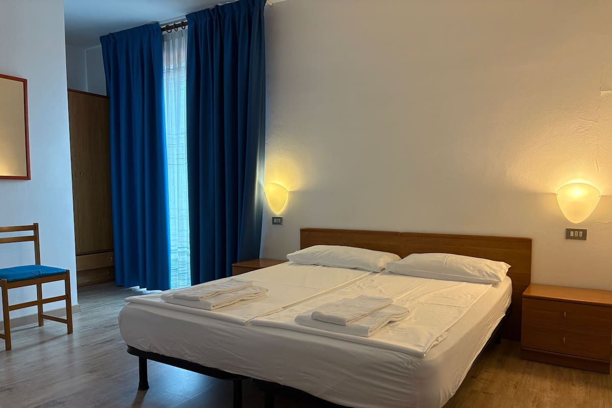 A hotel room with a large bed, two bedside tables, a chair, and a wardrobe.