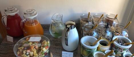 A kitchen counter with various food items and containers, including a fruit bowl, pitchers of beverages, and jars of grains and seeds.