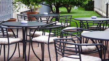A patio area with round tables and chairs, surrounded by a brick floor.