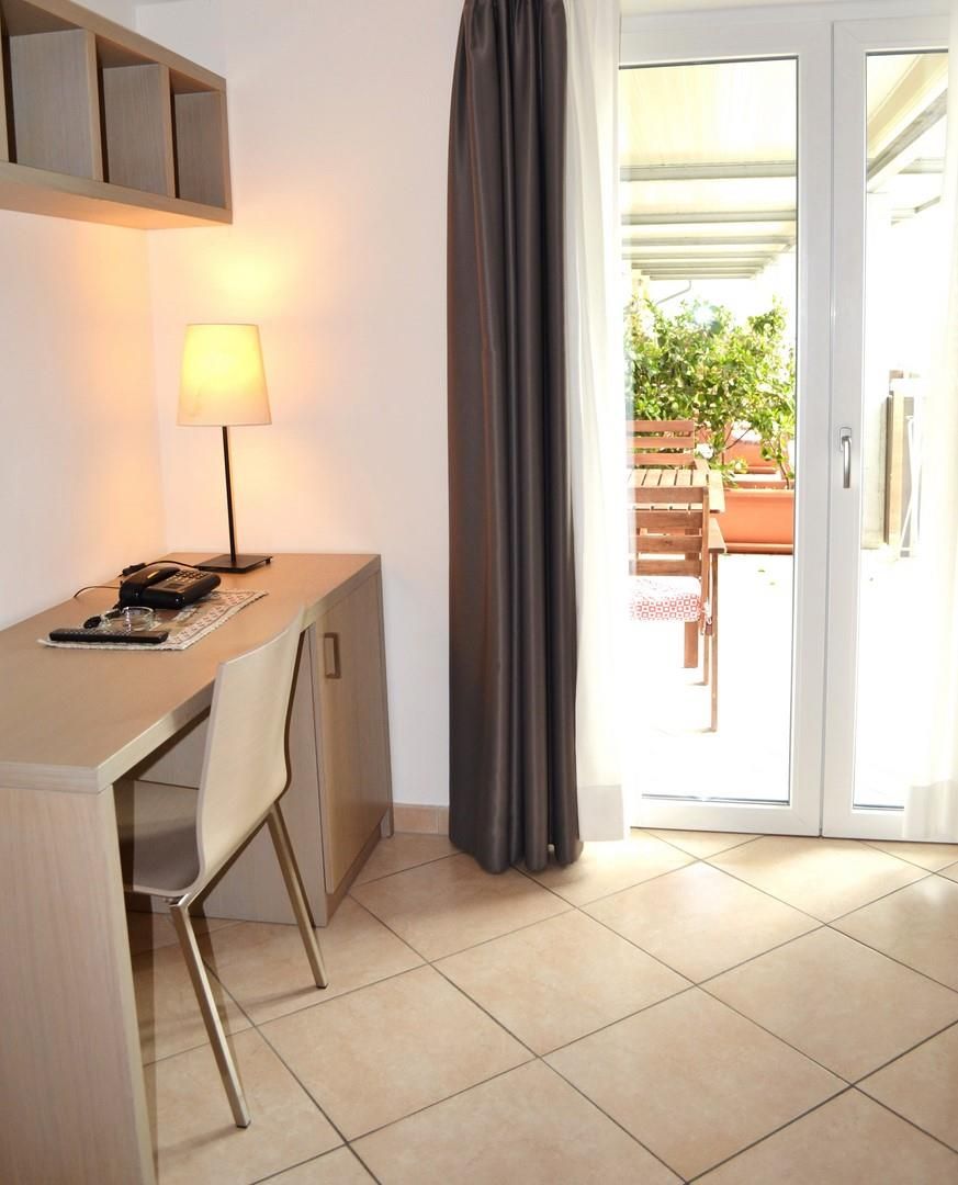 Una habitación pequeña con escritorio, silla, lámpara y puerta corrediza de vidrio que da a un área exterior.