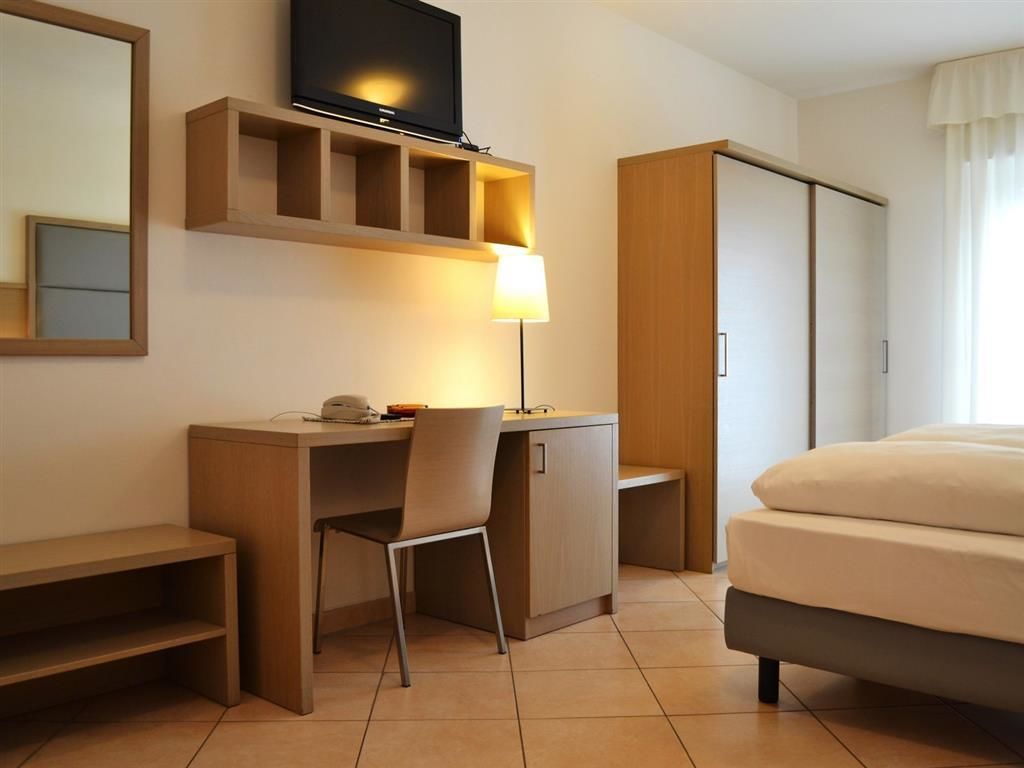 Ein Hotelzimmer mit Bett, Schreibtisch mit Stuhl, Fernseher, Lampe und Kleiderschrank.