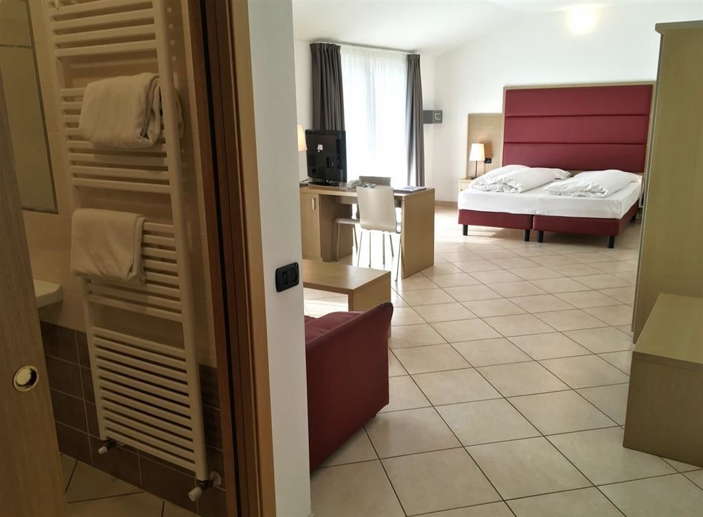 A hotel room with a bed, a desk, a chair, a TV, and a red couch.