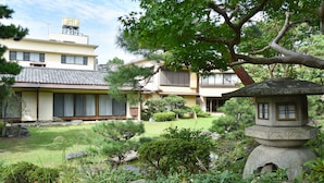 A traditional Japanese-style building with a tiled roof, surrounded by well-maintained gardens, including a stone lantern and various types of trees. - Hotel Hagoromo (Shizuoka)