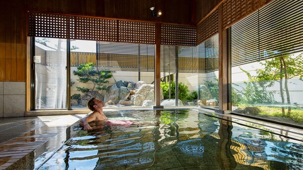 A person relaxing in a glass-bottomed indoor pool with wooden beams and large windows. - Hotel Hagoromo (Shizuoka)