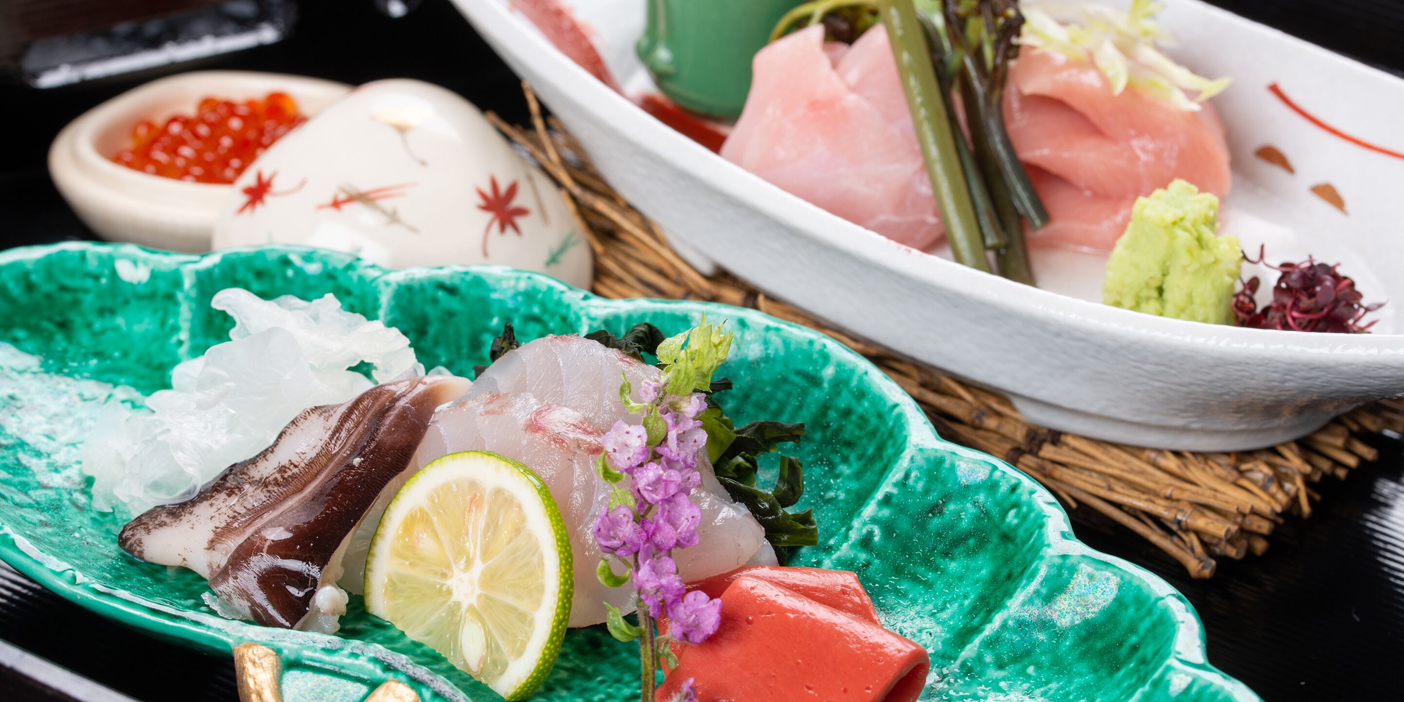A variety of sashimi and sushi on a table with a green plate and a white plate.