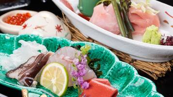 A variety of sashimi and sushi on a table with a green plate and a white plate.
