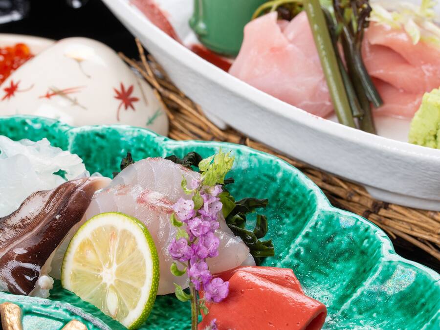 A variety of sashimi and sushi on a table with a green plate and a white plate.