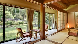 A traditional Japanese room with tatami flooring, a low table, and a view of a garden through large sliding doors. - Hotel Hagoromo (Shizuoka)