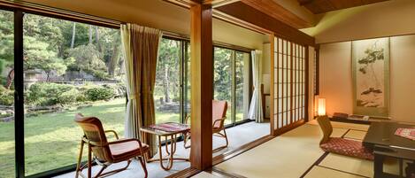 A traditional Japanese room with tatami flooring, a low table, and a view of a garden through large sliding doors.