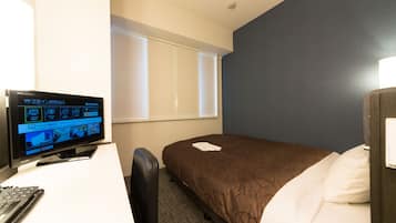 A hotel room with a bed, a desk with a computer, and a window with blinds.