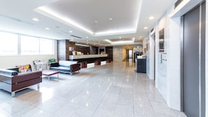 A modern lobby with a reception desk, seating area, and a kitchen in the background. - Sanco Inn Shizuoka Kitaguchi (Shizuoka)