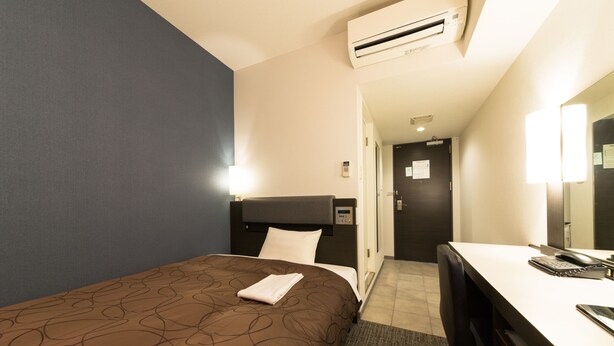 A hotel room with a bed, a desk with a computer, a chair, and an air conditioning unit. - Sanco Inn Shizuoka Kitaguchi (Shizuoka)