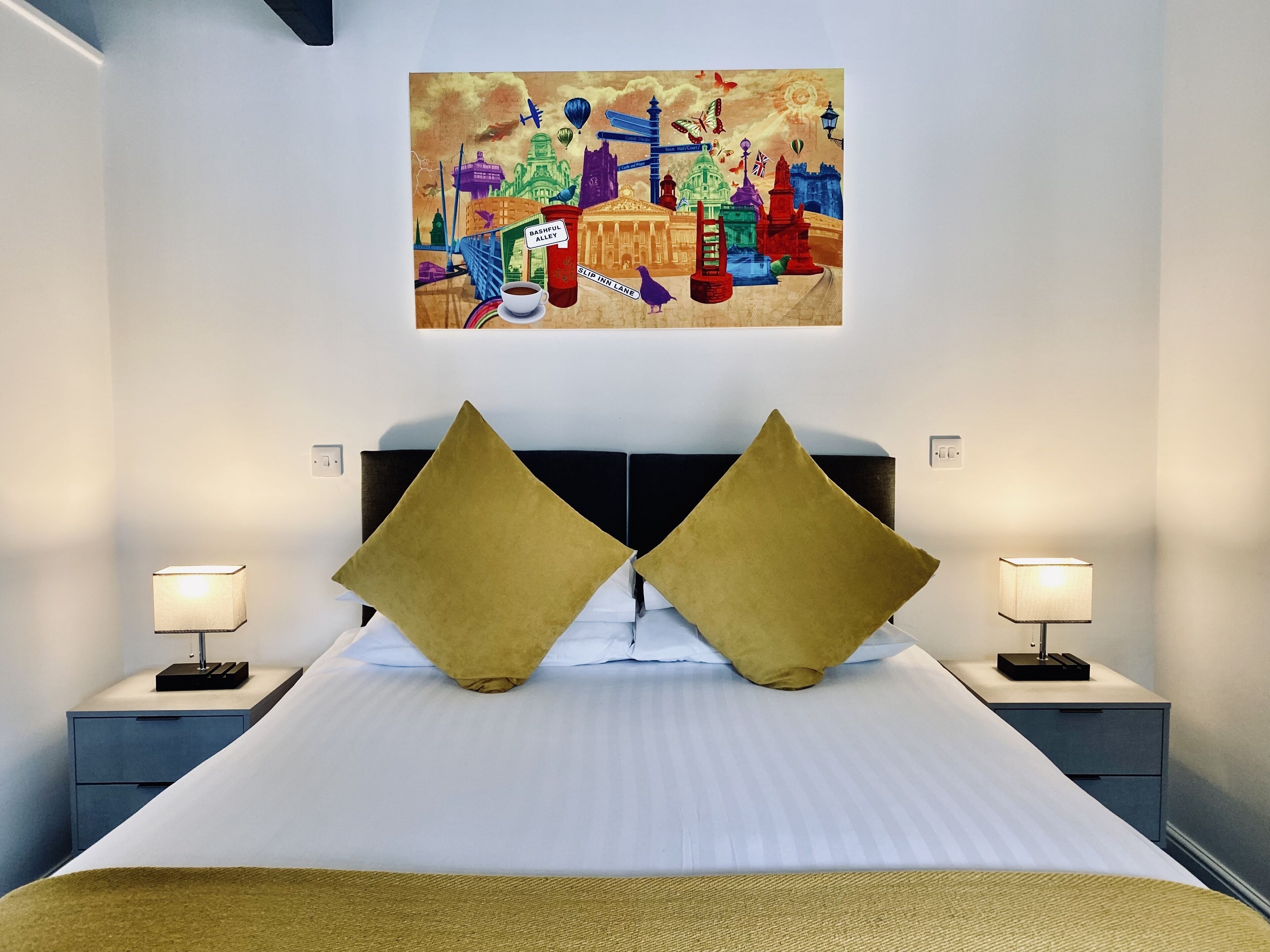 A hotel room with a large bed, two nightstands with lamps, and a colorful artwork on the wall.