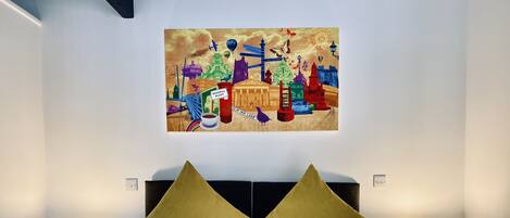 A hotel room with a large bed, two nightstands with lamps, and a colorful artwork on the wall.