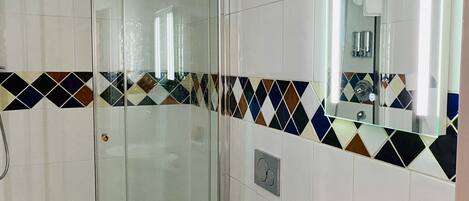 A modern bathroom with a glass shower enclosure, a white sink with a mirror, and a patterned tile border.