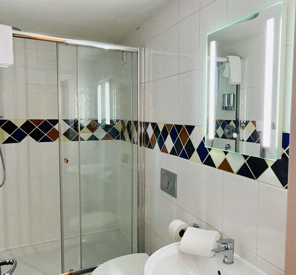 Un baño moderno con cabina de ducha de vidrio, un lavamanos blanco con espejo y un zócalo de baldosas con diseño.