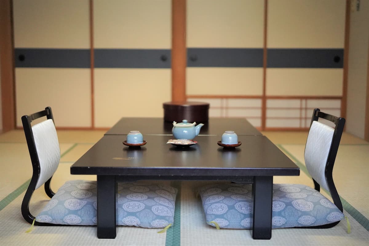 Una habitación japonesa tradicional con suelo de tatami, una mesa baja y dos sillas con cojines.