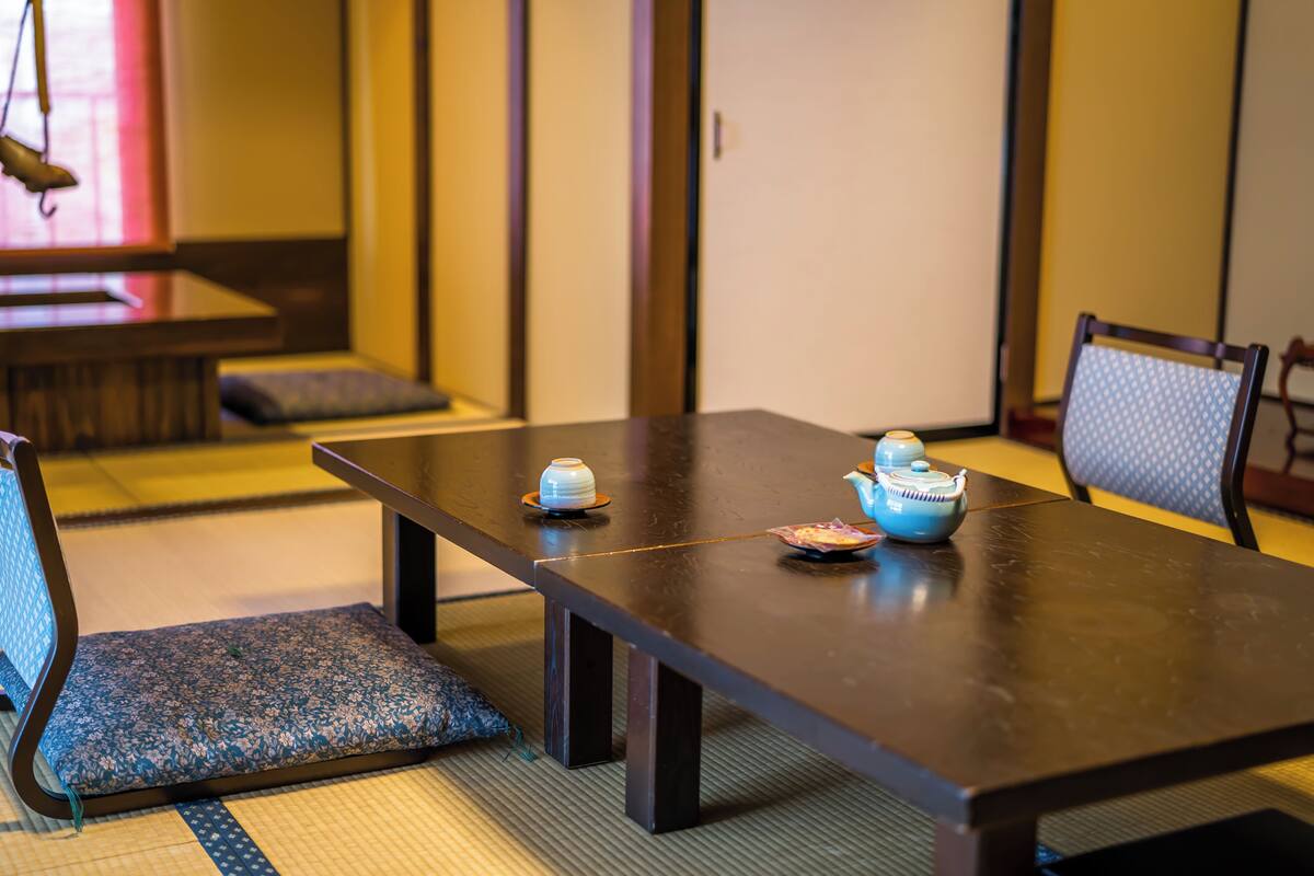 Una habitación tradicional japonesa con suelo de tatami, una mesa baja con un juego de té y un banco acolchado.