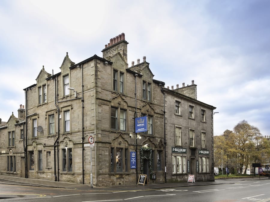 Un edificio histórico de piedra con varias ventanas y un letrero que dice 'J. Balshaw'.