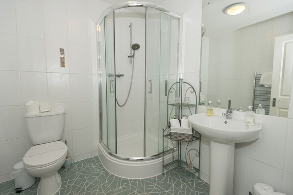 A modern bathroom with a glass-enclosed shower, a white toilet, and a pedestal sink.