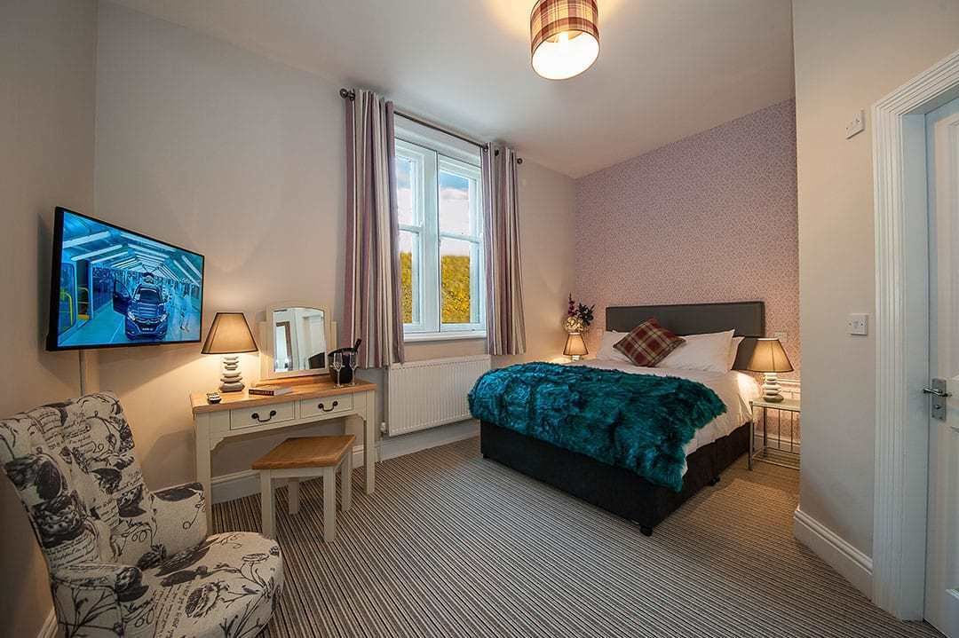 Camera d'albergo con un letto, una scrivania, una sedia, una televisione e una finestra con tende.