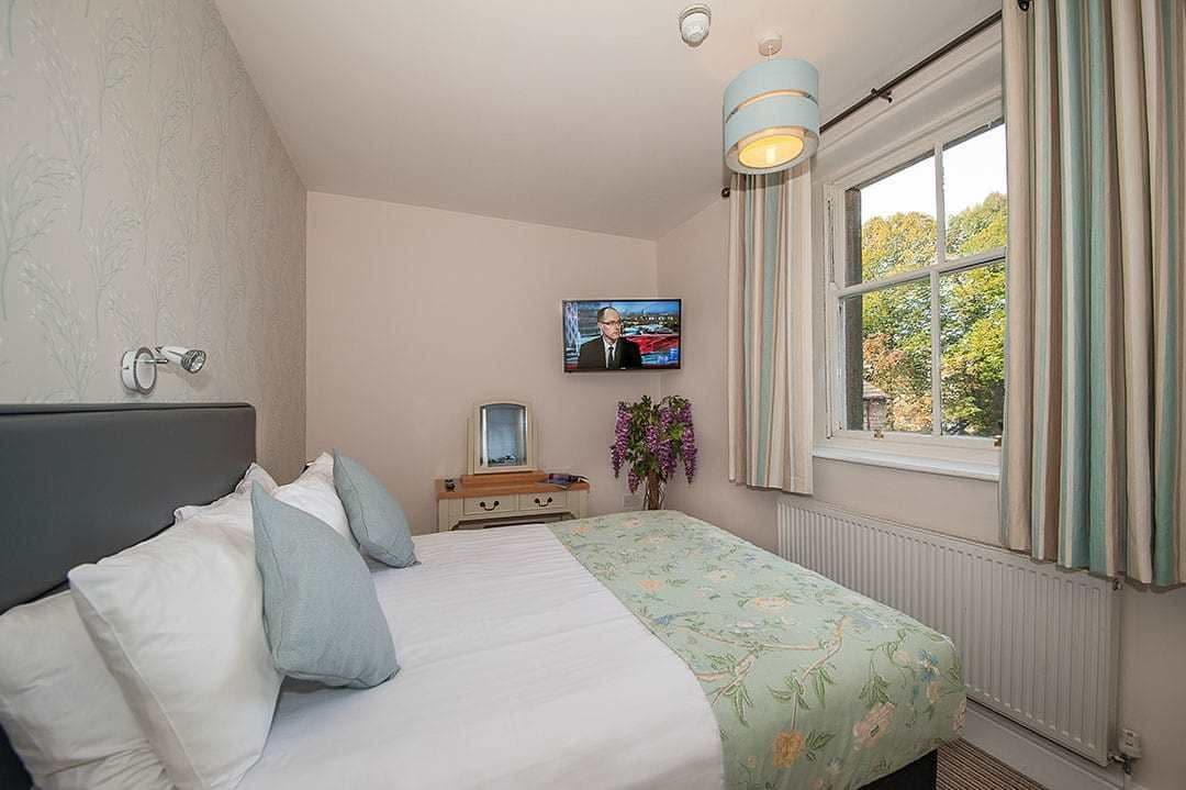 A bedroom with a bed, a TV, a dresser, and a window with curtains.