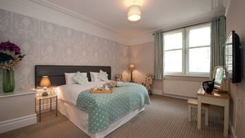 A neatly arranged bedroom with a bed, bedside lamps, a small table with a tray, and a window with curtains.