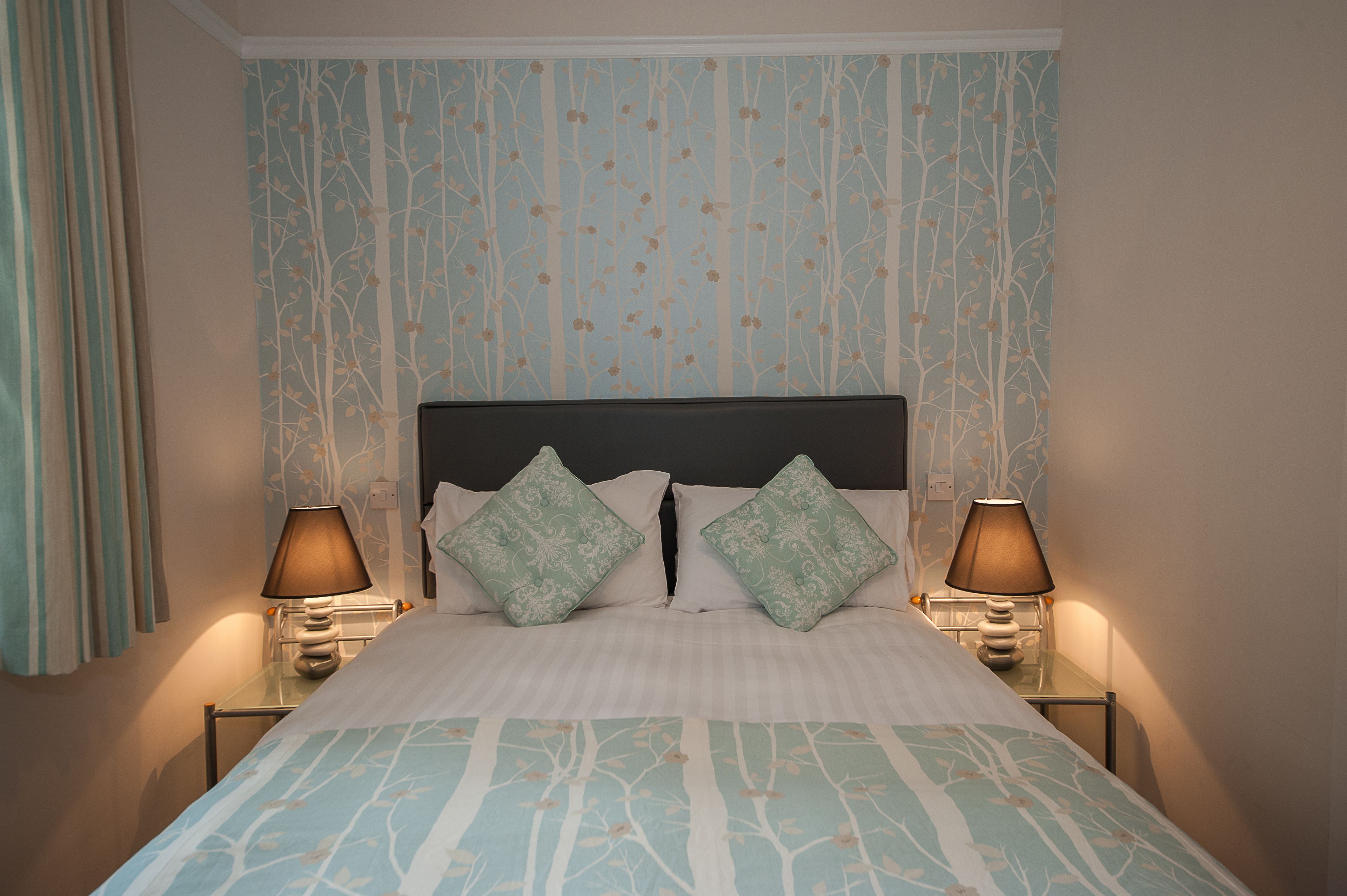 A neatly made bed with a patterned bedspread, two matching pillows, and two bedside lamps.