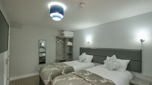 A hotel room with two beds, a wardrobe, a mirror, and a bedside table. - The Royal Hotel and Bar (Lancaster)