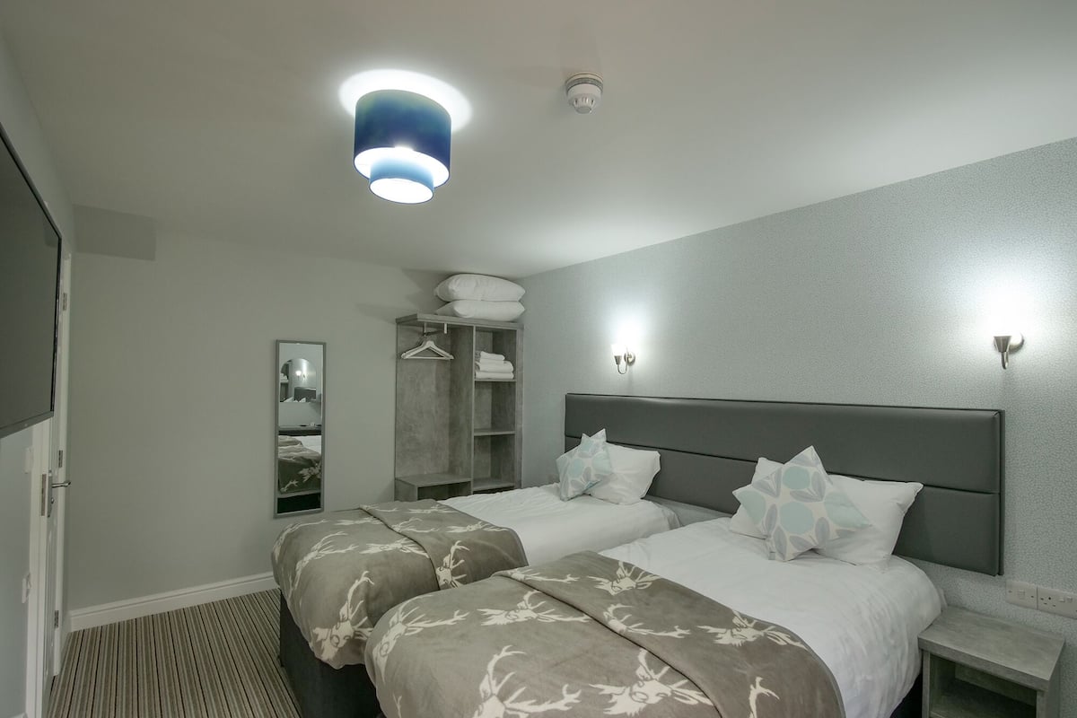 A hotel room with two beds, a wardrobe, a mirror, and a bedside table.