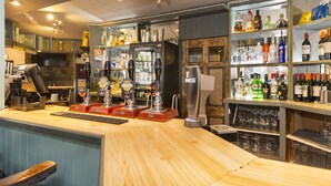 A bar area with a wooden counter, multiple taps, and shelves stocked with bottles. - The Royal Hotel and Bar (Lancaster)