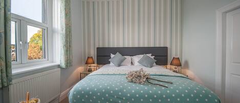 A bedroom with a bed, two bedside tables, a window with curtains, and a radiator.