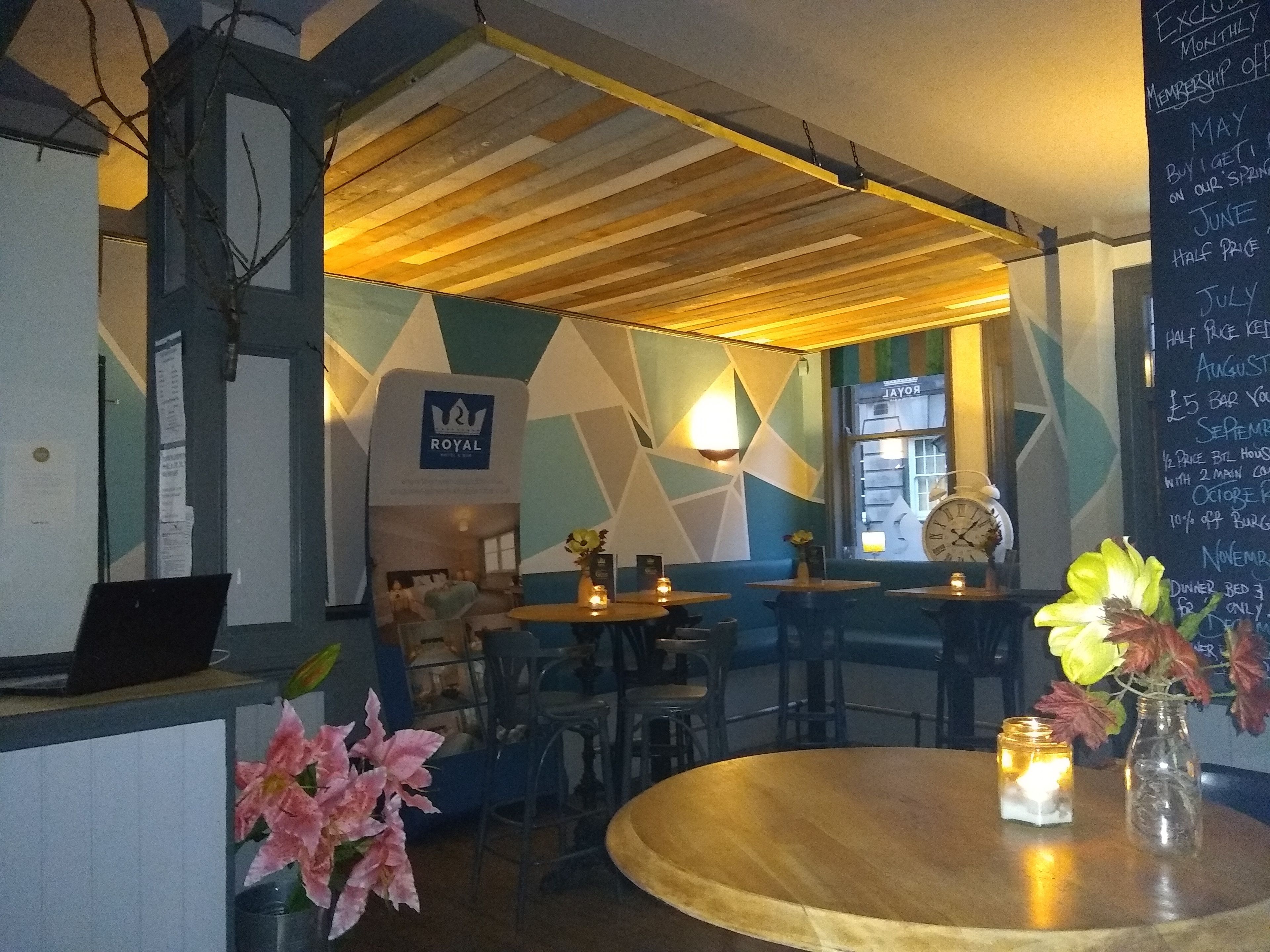 A cozy restaurant interior with a geometric wall design, a wooden ceiling, and a chalkboard menu.