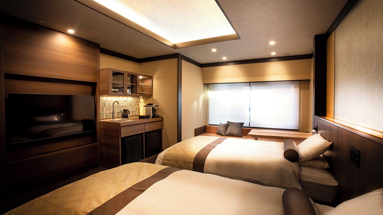 Une chambre d’hôtel moderne équipée de deux lits, d’une kitchenette, d’une grande fenêtre et d’un téléviseur à écran plat.