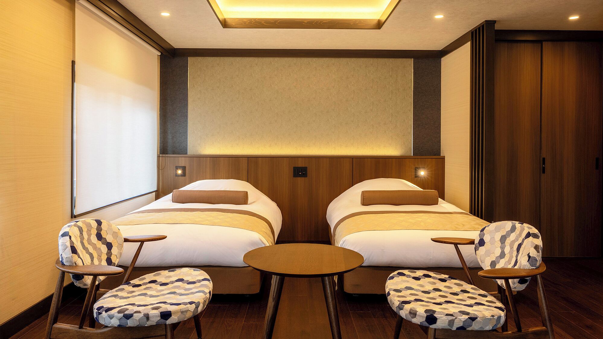 Une chambre d’hôtel avec deux lits, une petite table, deux chaises et une grande fenêtre.
