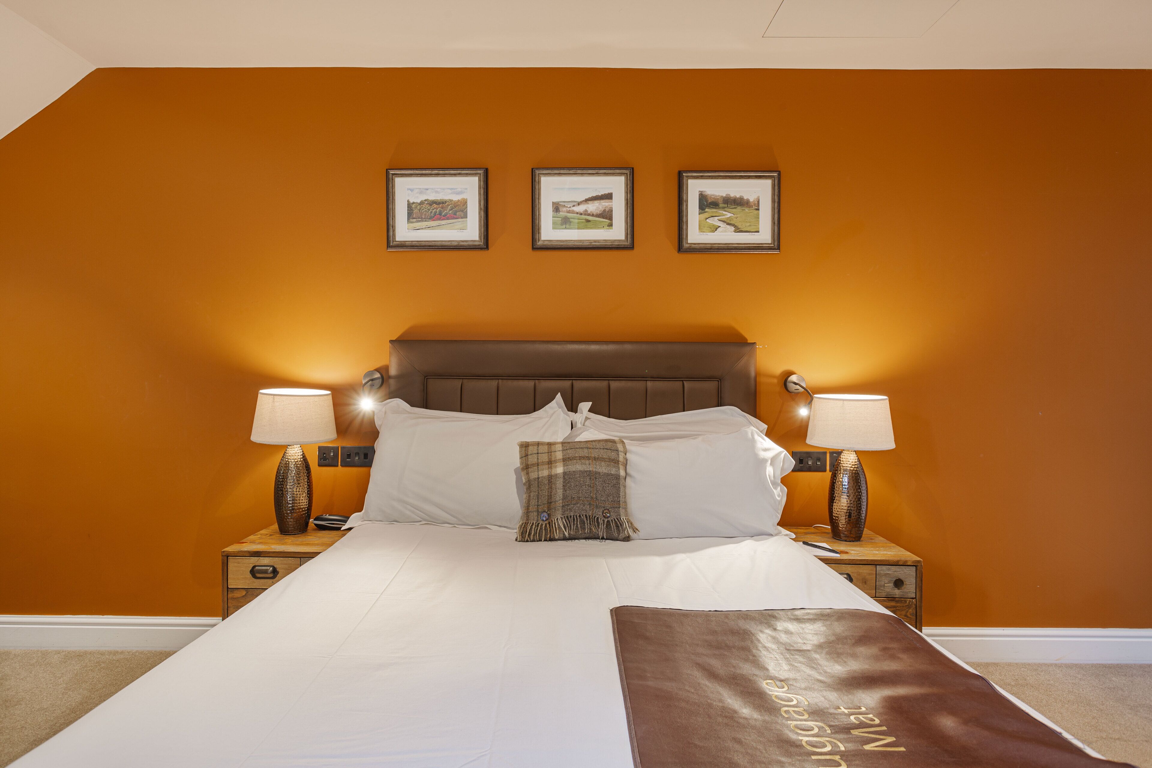 Habitación de hotel con una cama grande, dos mesitas de noche con lámparas y tres cuadros enmarcados en la pared.