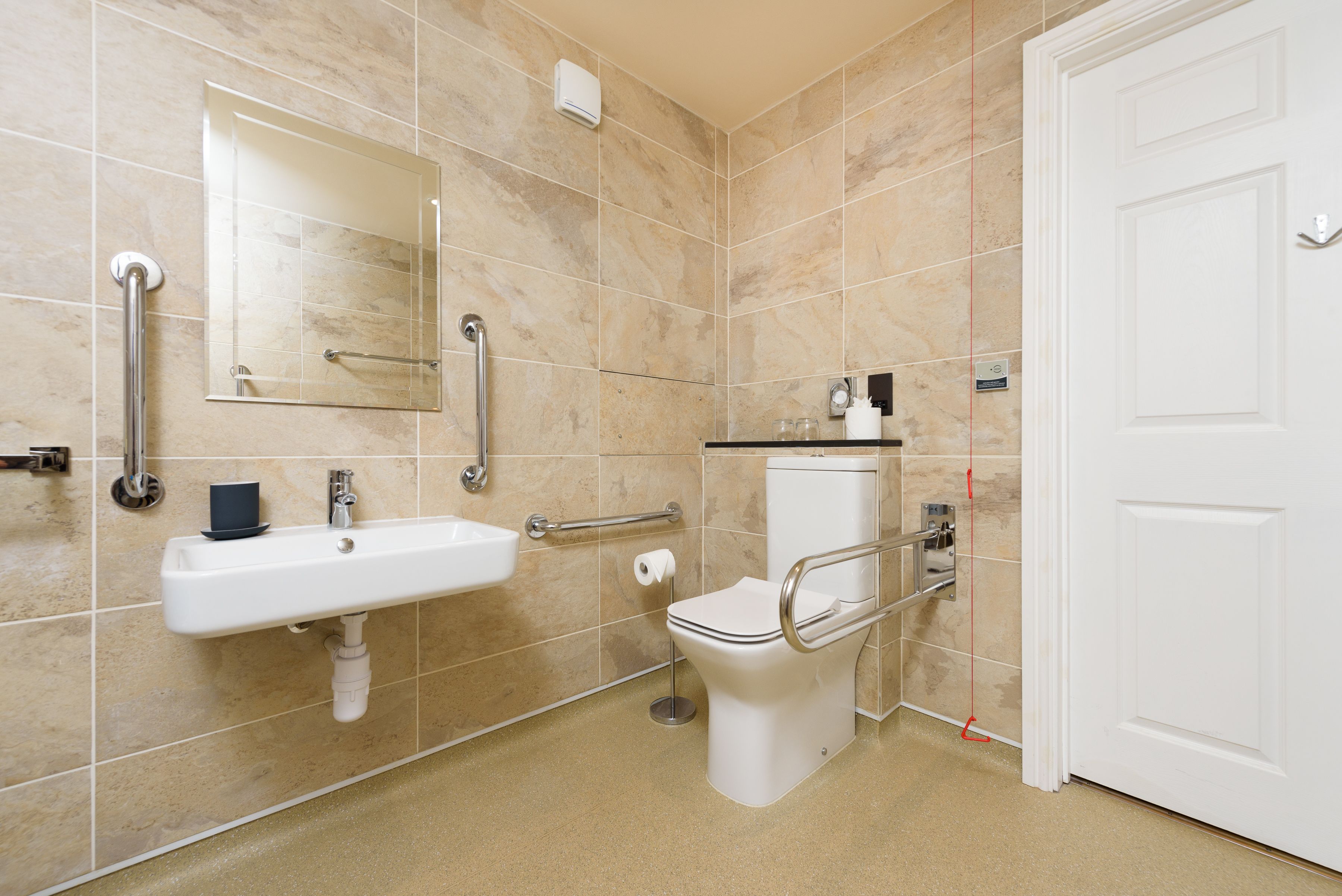 Une salle de bain équipée d’un lavabo, d’un miroir, de toilettes et de barres d’appui.
