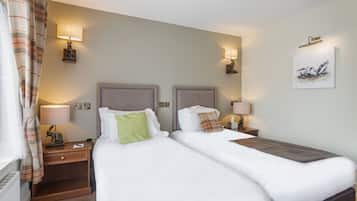 Habitación de hotel con dos camas, mesitas de noche con lámparas, una obra de arte colgada en la pared y una ventana con cortinas.