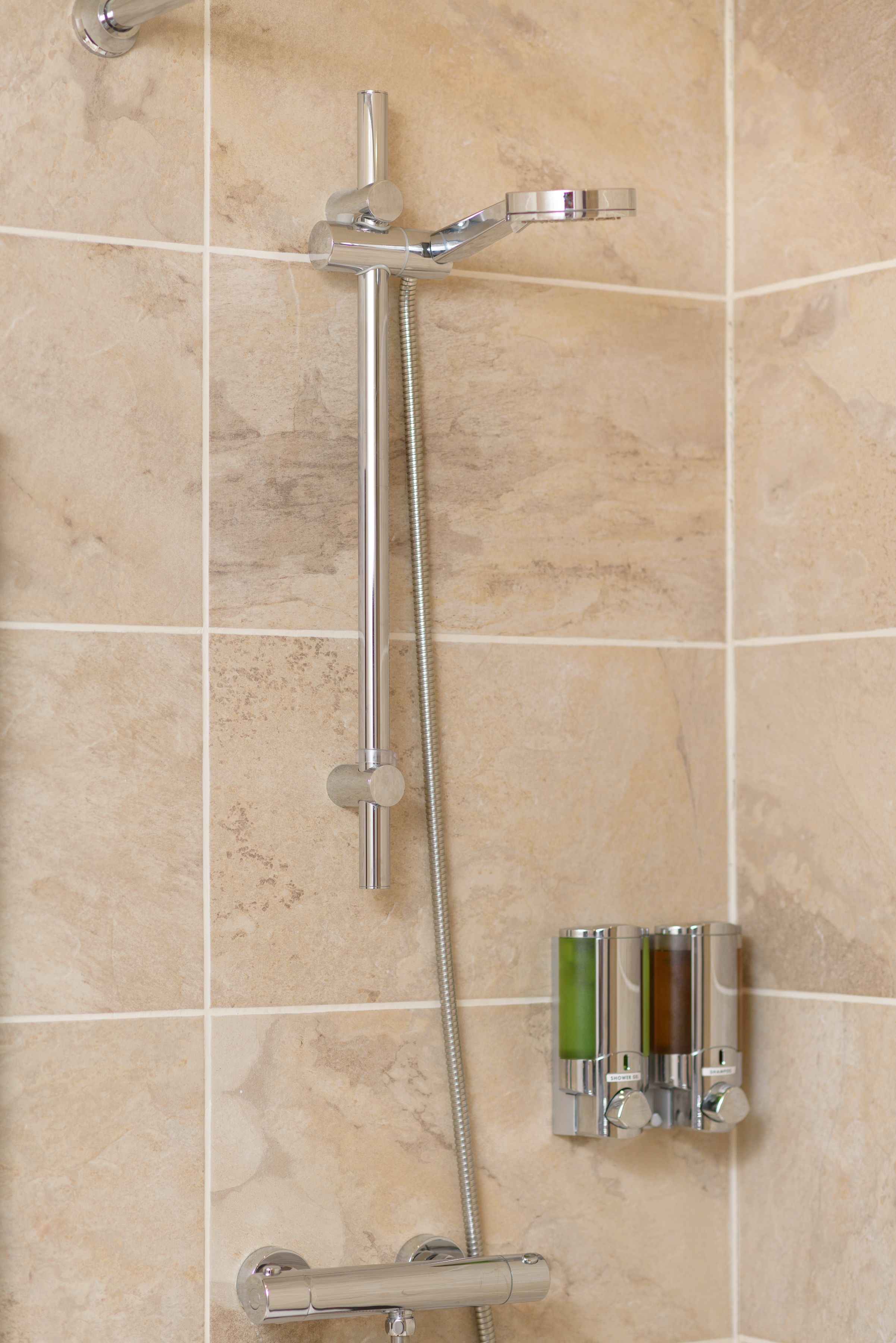 Une douche équipée d’un robinet chromé, d’un pommeau de douche à main et d’un distributeur de savon mural.