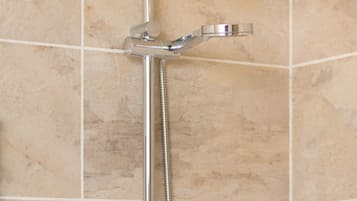 A shower with a chrome faucet, a handheld showerhead, and a wall-mounted soap dispenser.