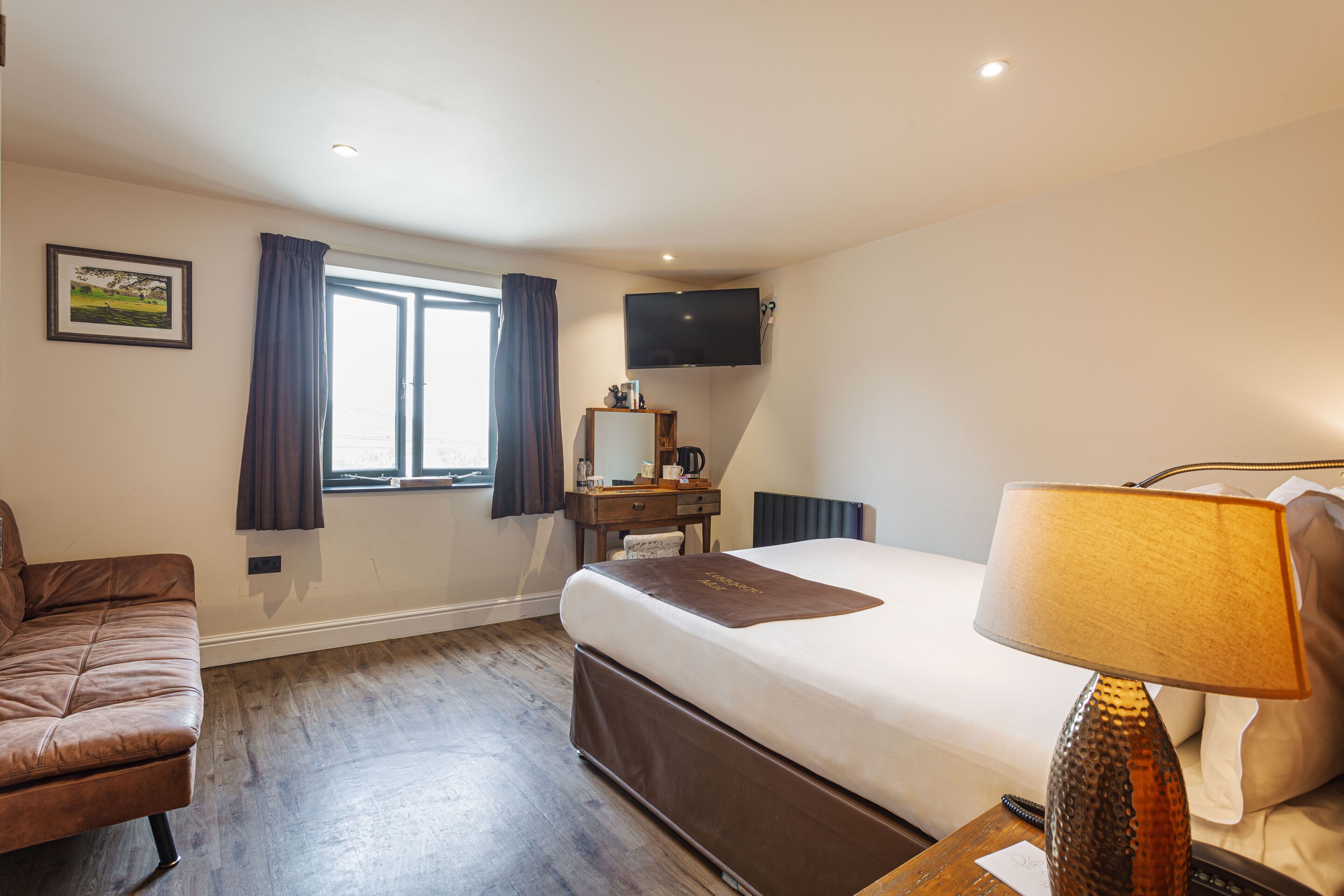 Habitación de hotel con cama, escritorio, silla, televisor montado en la pared y ventana con cortinas.