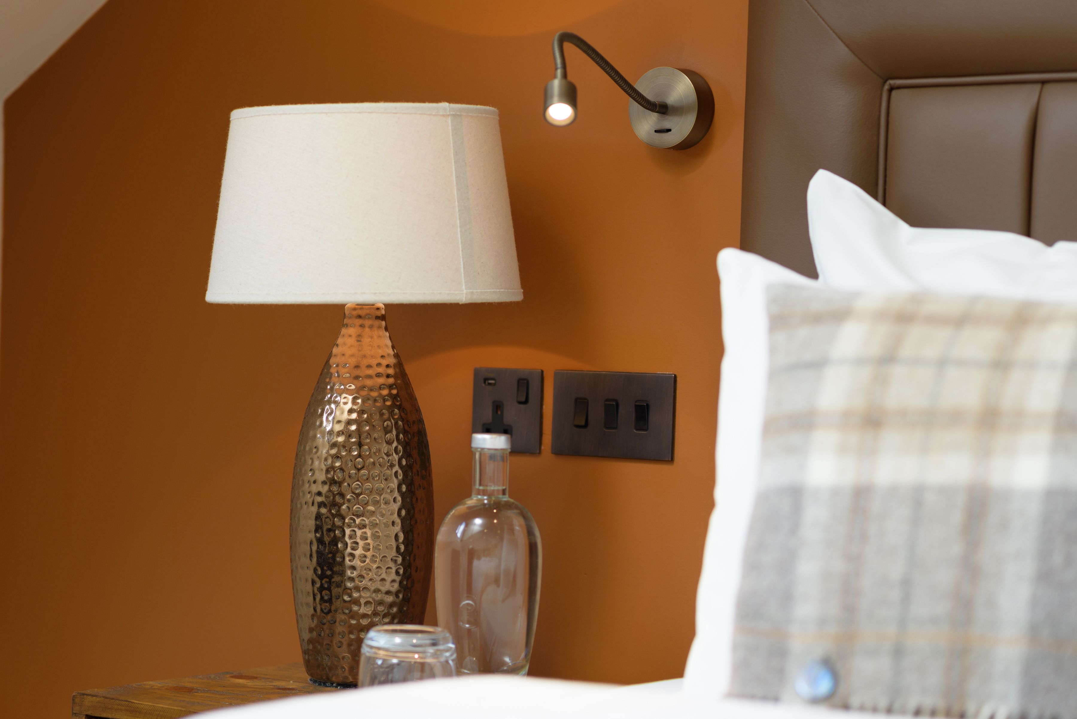 A hotel room with a lamp, a bottle, and a power outlet on the wall.