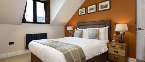 A bedroom with a large bed, two bedside lamps, a nightstand, and a window with curtains.