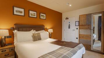 A hotel room with a large bed, two bedside tables, a wooden wardrobe, and a door with a mirror.