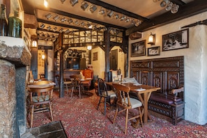 A traditional pub interior with wooden furniture, a patterned carpet, and a variety of metal mugs hanging from the ceiling.