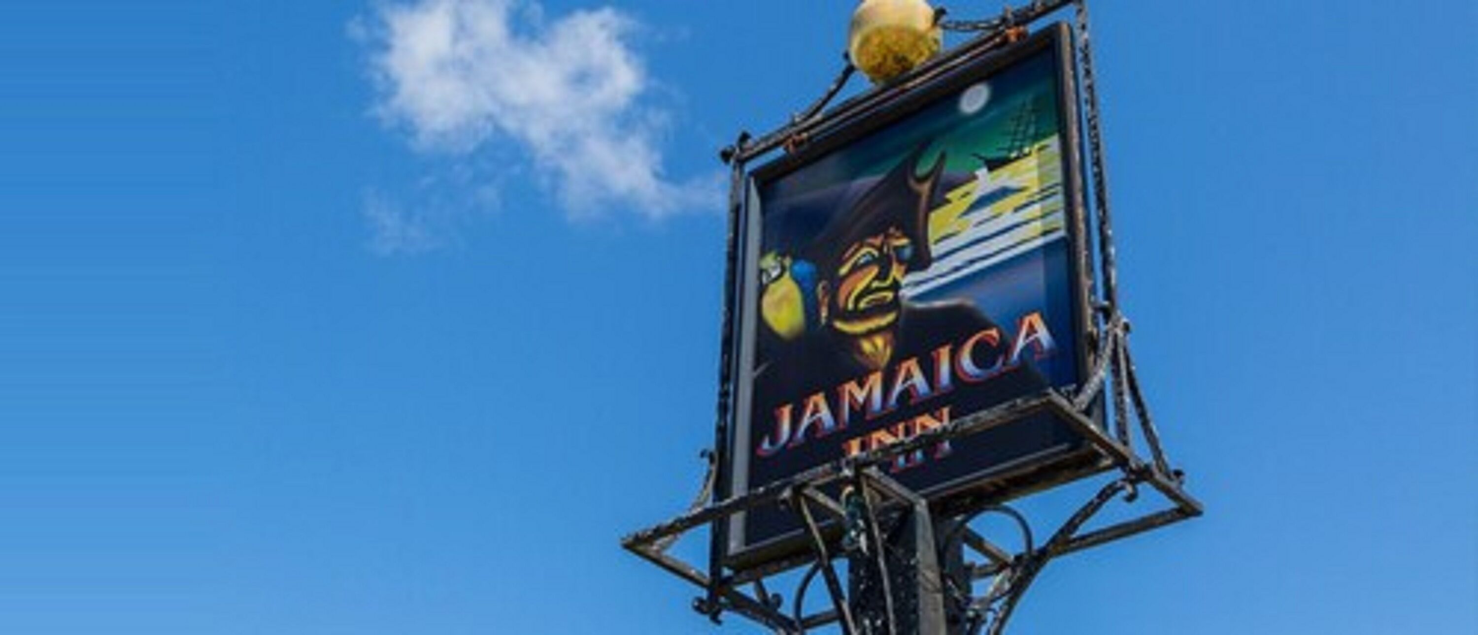 A sign for Jamaica Inn with a clear blue sky in the background.