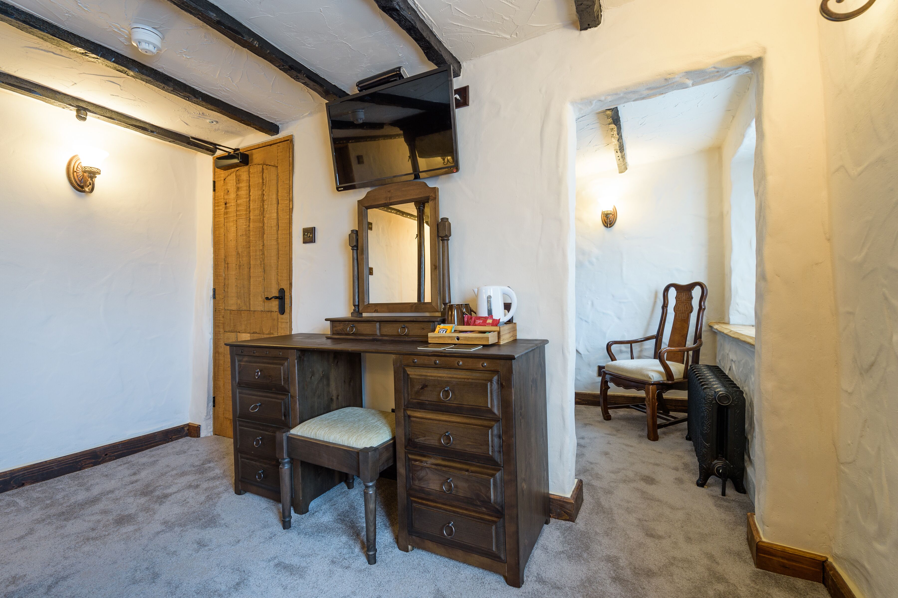 A room with a wooden desk, a chair, a mirror, and a radiator.